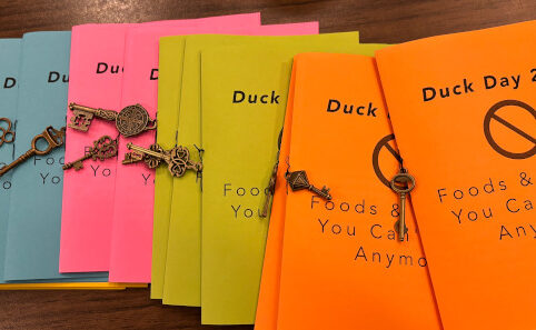 Bright colored booklets that say Duck Day 2024 with a small brass key dangling from each one.