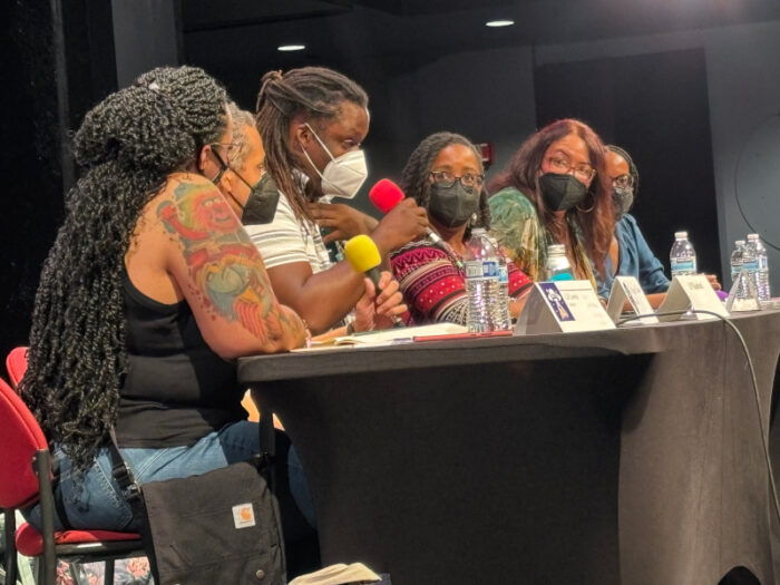 Six panelists at a table seen from the side. All six are Black or mixed race. Pictured are LD Lewis (Moderator), Christopher Caldwell, LP Kindred, Rebecca Roanhorse, Erin Roberts, and Nicole Glover.