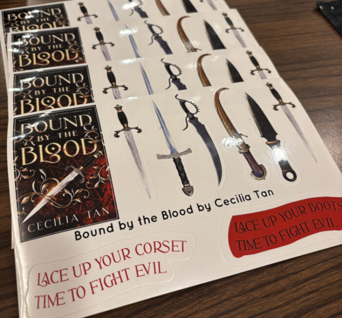 ALT
03:57 PM
Jan 09, 2026
Photo of stickers showing the book cover of Bound by the Blood, lots of pretty knives and daggers, and slogan stickers saying Lace up Your Boots, it's time to fight evil, and Lace up your corset, It's time to fight evil.