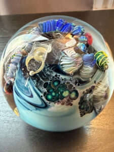 A clear glass globe around the size of a baseball with colored glass inside it making it look like an aquarium or a view into an alien planet. Glass planet by artist Josh Simpson